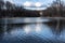 Water landscape in riparian forest with reflection of big gray and white clouds in the glittering water