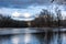 Water landscape in riparian forest with reflection of big gray and white clouds in the glittering water