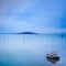 Water, poles, island and rock in a blue morning on lake. Hills on background