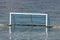 Water polo goal with white frame and blue net supported with rope and floating buoys resting on calm sea