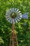 Water pumping windmill with metal vanes on the background of green trees