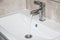 Water runs from the tap into the sink. Modern water tap in the bathroom with running flowing water in sink. Open chrome sink