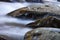 Water rushing around three large rocks in a cold mountain stream