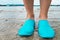 Water shoes / blue swimming shoes on rocks in water on beach. Closeup detail of the feet of a woman wearing water shoes standing