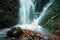 Water spray below small waterfall on mountain stream, water is falling over mossy boulder. The spray create on level and gravel mi