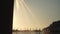 Water spraying from beach shower head, morning sun lit blurred background, anonymous person reaching hands up to stream, closeup