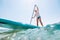 Water surface-level view angle to the smiling blonde teenager boy rowing stand up paddle board. Active family summer vacation time