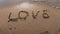 Water washes away the word love in the sand