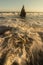 Water waves crashing onto shore of beach with tall, pointy rock and bird perched