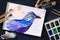 Watercolor painting of blue bird and artistic tools on table