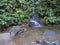 Waterfall cascade falling on stone and lush vegetation on hiking trail Janela do inferno, in fainforest Sao Miguel