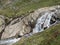 Waterfall cascade at wild Freigerbach stream with rocks, green meadow and blooming alpenrose, Rhododendron ferrugineum