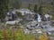 Waterfall cascade on wild river stream studeny potok with boulders, autumn colored tree at mountain valley Velka Studena