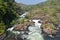 Waterfall dam rocks Tower building landscape on banks of river in a vast area with bushes sky horizon seen far away