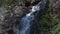 Waterfall falls in cascade in mountain gorge.