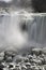 Waterfall flowing over snow covered rocks, mist rising, frost co