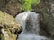 Waterfall hidden in forest and stones. Splashes of pure mountain water