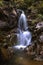Waterfall with long exposure surrounded by rocks. Smoothly Flowing Stream Of Water In The Woods. Water flowing in wild creek. Wild