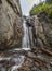 Waterfall in the mountains of Altai. Rocks, stormy stream, tree roots