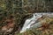 Waterfall in nature pine Scandinavian mountain forest in evening light. Wet cold rock stones covered with northern moss. Nordic sp