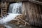 Waterfall near a log wall and a wooden staircase.