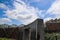 A waterfall over a stone wall with a doorway on a curved footpath in the garden with blue sky and powerful clouds