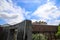 A waterfall over a stone wall with a doorway on a curved footpath in the garden with blue sky and powerful clouds