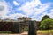 A waterfall over a stone wall with a doorway on a curved footpath in the garden with blue sky and powerful clouds