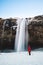 Waterfall in winter, photographer in red jacket standing alone on the snow at Seljalandsfoss waterfall in Iceland