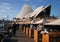 Waterfront promenade walk with wood tables, white umbrellas, stools and chairs for outdoor dining at Sydney Opera House, Australia