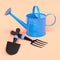 Watering can with garden tools like shovel, rake and fork on orange background