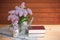 Watering cans with branches of lilac and books on wooden table