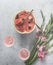 Watermelon cocktails with sparkling wine in wine glasses, sliced watermelon and pink flowers on pale grey concrete kitchen table.