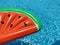 Watermelon pool float, part of ring floating in a refreshing blue swimming pool
