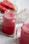 Watermelon smoothie in glass jars with fresh slices of water melon over white wooden table, side view.