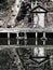 A waterside run down wooden jetty with a small shack and tree reflected in the still water