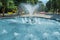 Waterworks fountain with water sprays and geysers in park or garden. Summer day time freshness and relax concept. Blue aqua pool