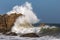 Wave breaking against giant rock offshore, spray high in the air.