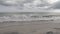 Wave breaking on the beach in slow motion, ocean and cloudy gray sky. Calm, serene, sad atmosphere.