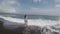 The wave breaks down on the shore and large sprays fly over the girl in black sand beach