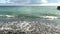 Wave with foam runs on the beach with pebbles on the background of the sea and the sky with clouds