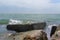 The wave is lapping over a square rock on the pier covered in green algae. Square-like rock in Sunny day. The emerald-colored sea