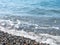 Wave on a pebbly shore. Sea foam. Bathing place. Nature of the south. Close-up of the coastline