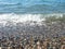 Wave on a pebbly shore. Sea foam. Beautiful pebble beach. Close-up of the coastline