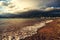 A wave runs over the pebbly beach of the resort town. Sea foam, pebbles. In the background, mountains covered with