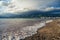 A wave runs over the pebbly beach of the resort town. Sea foam, pebbles. In the background, mountains covered with