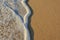 Wave of the sea entering the sand of the beach forming foam, contrast of white and beige. Macro photography