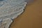 Wave of the sea entering the sand of the beach forming foam, contrast of white and beige. Macro photography