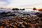 Wave in the shallow sea and a sunlit pebble beach at sunset