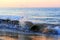 Wave splashing on stones on beach in sunrise